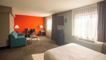 Hotelkamer met een bed, bureau, stoel, televisie en raam met gordijnen.