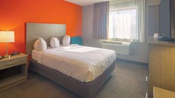 Een hotelkamer met een groot bed, een bureau, een lamp en een airconditioner.
