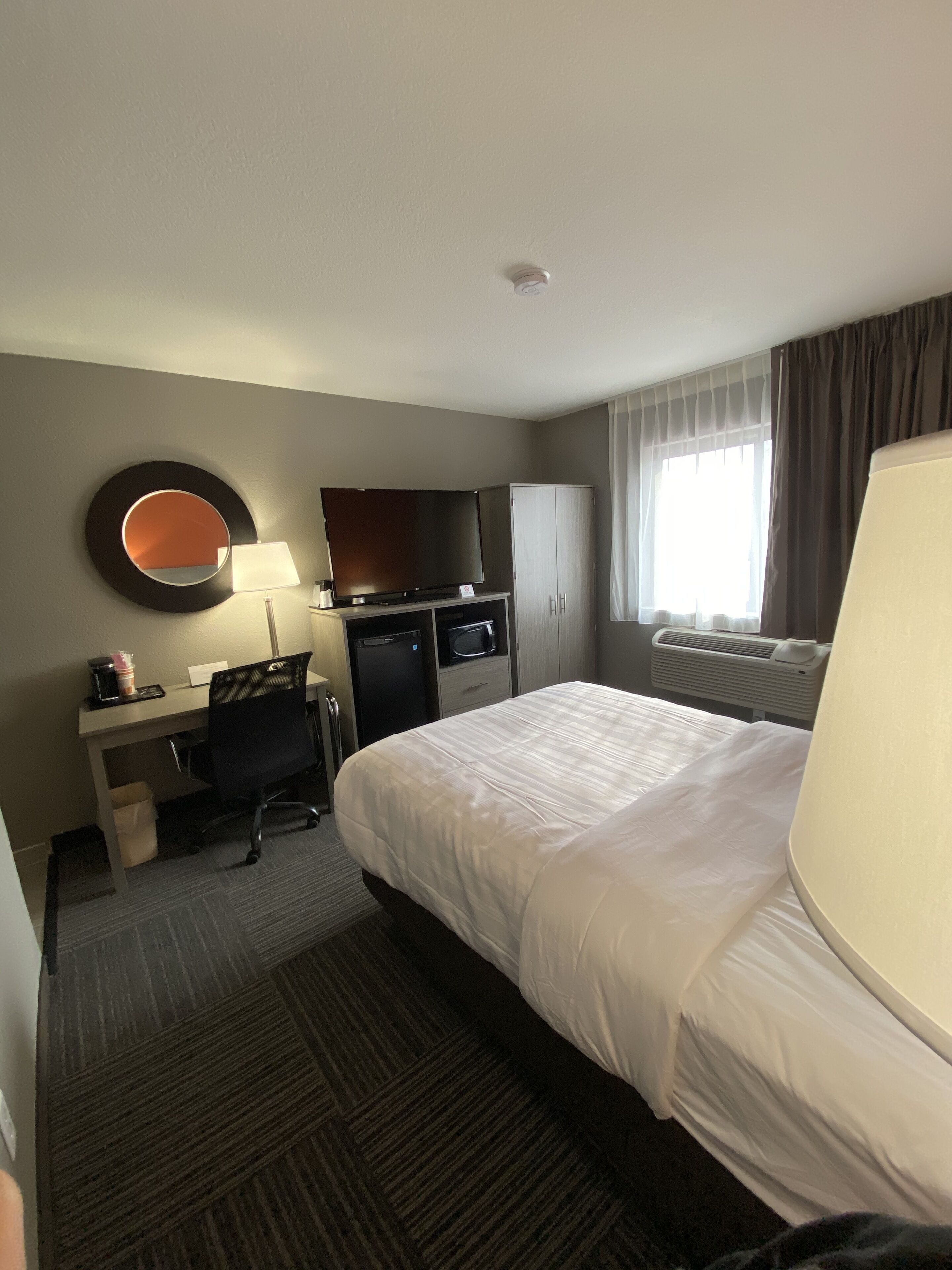 Quarto de hotel com cama, escrivaninha com computador, televisão e espelho na parede.