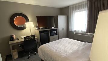 Quarto de hotel com cama, escrivaninha com computador, televisão e espelho na parede.