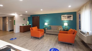 Un vestíbulo de hotel con dos sillones naranja, un sofá, una recepción y un equipo de aire acondicionado instalado en la pared.
