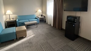 Habitación de hotel con sofá azul, una mesita, televisor y televisor de pantalla plana montado en la pared.