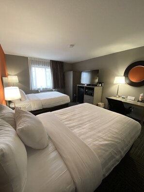 A hotel room with two beds, a desk with a computer, a TV, and a mirror.
