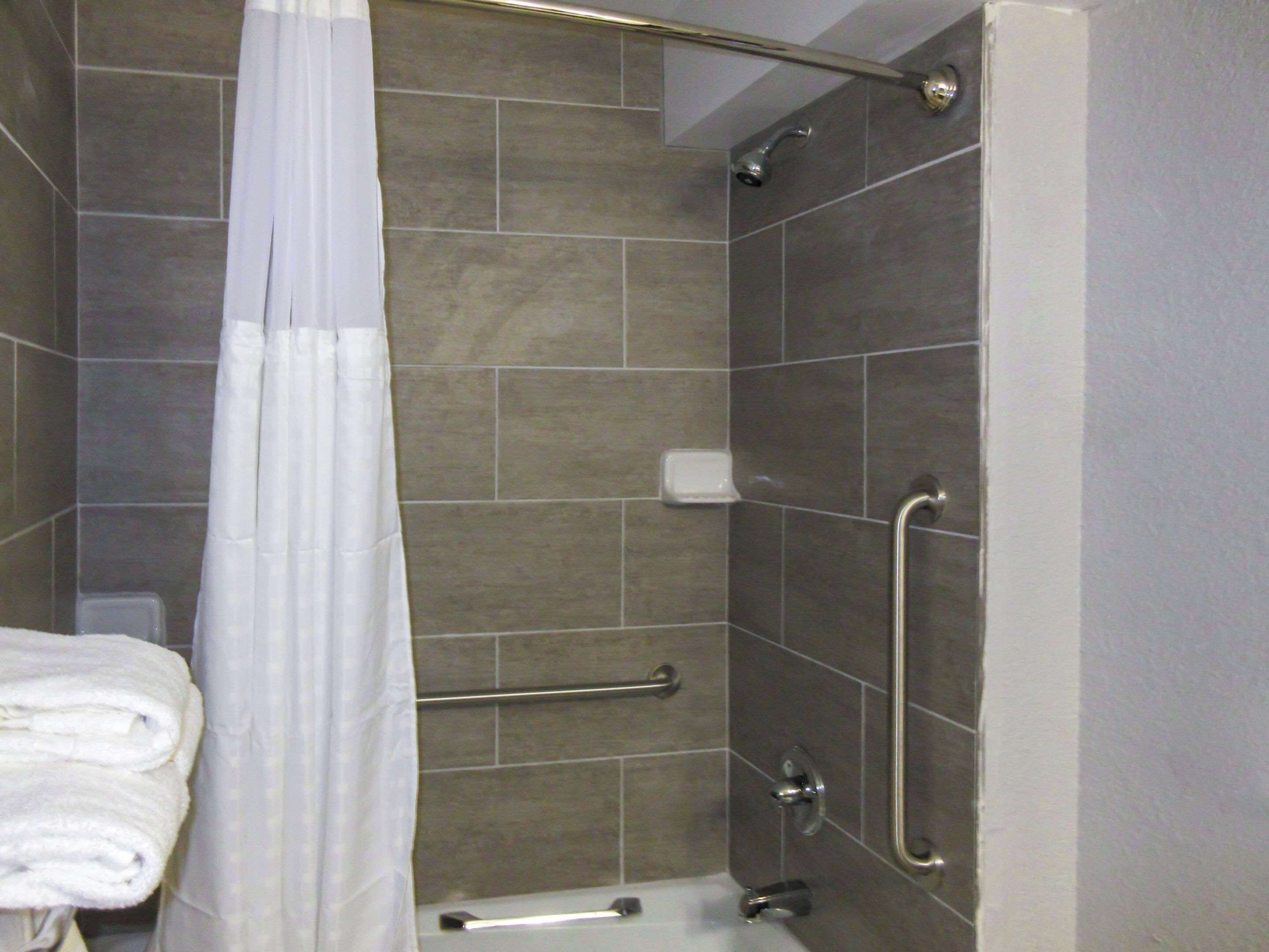 A shower area with a grab bar, a white towel, and a soap dish.