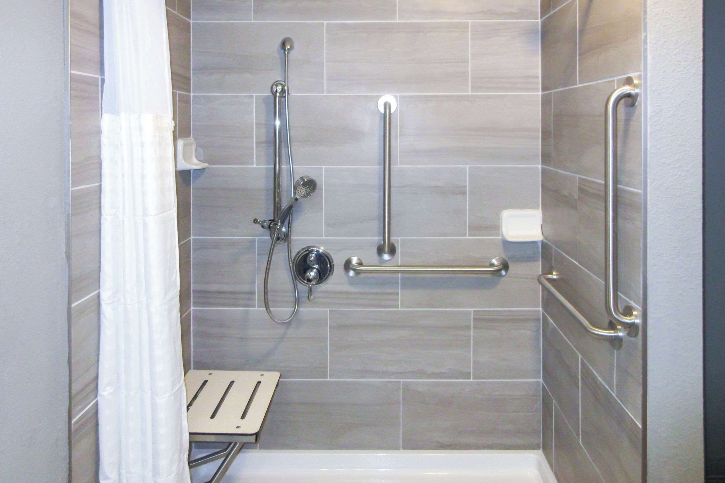 A shower area with a grab bar, a handheld showerhead, and a handheld faucet.