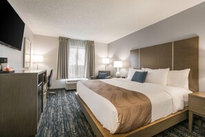 A hotel room with a large bed, bedside tables, a desk with a chair, a flat-screen TV, and a window with curtains.