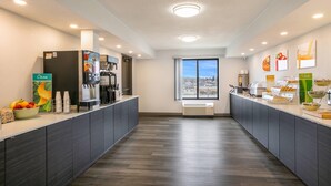Un área de cocina limpia y moderna con estación de café, frutero y vistas a través de un gran ventanal.