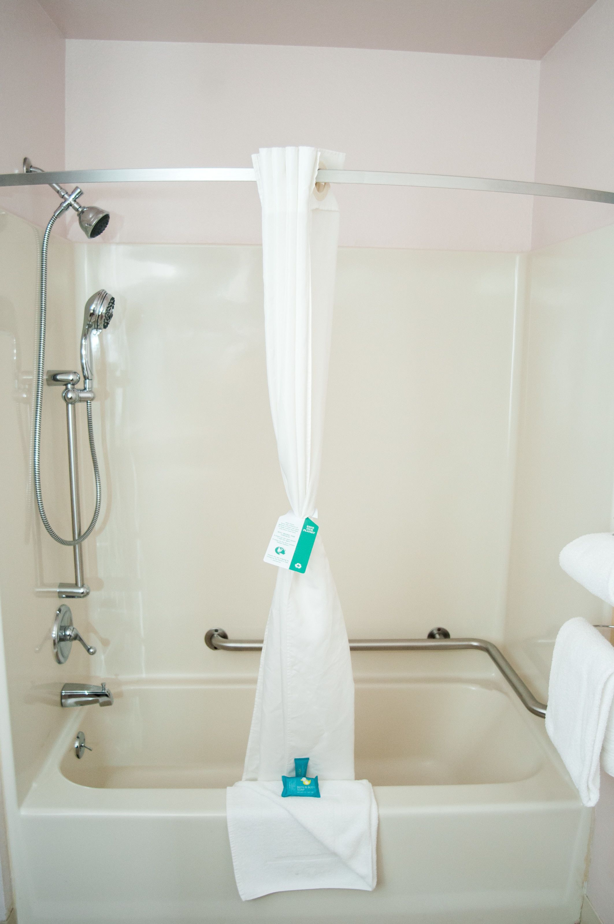 A bathtub with a showerhead, grab bars, and a white curtain.