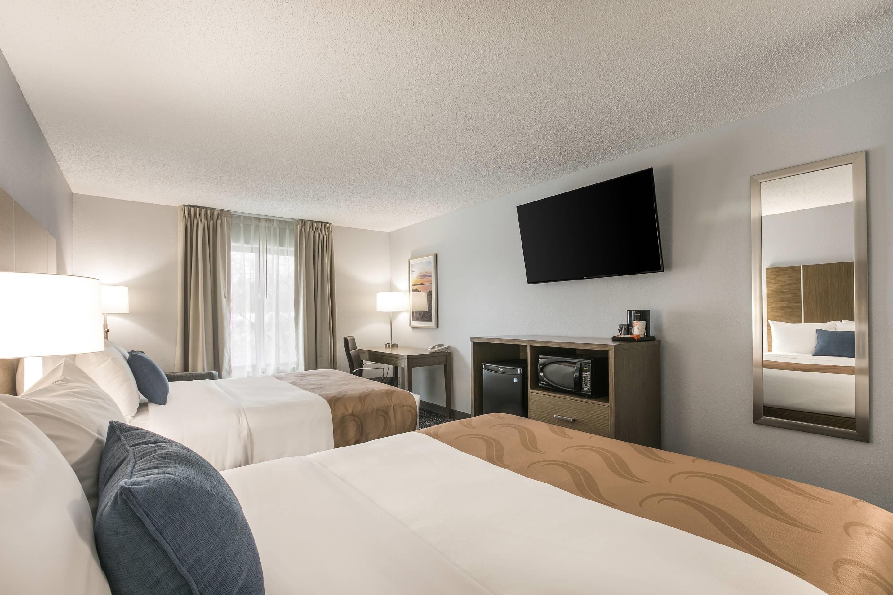 A hotel room with two beds, a desk, a television, and a mirror.