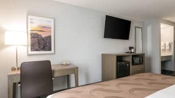 A hotel room with a bed, desk, chair, TV, and a small kitchenette.