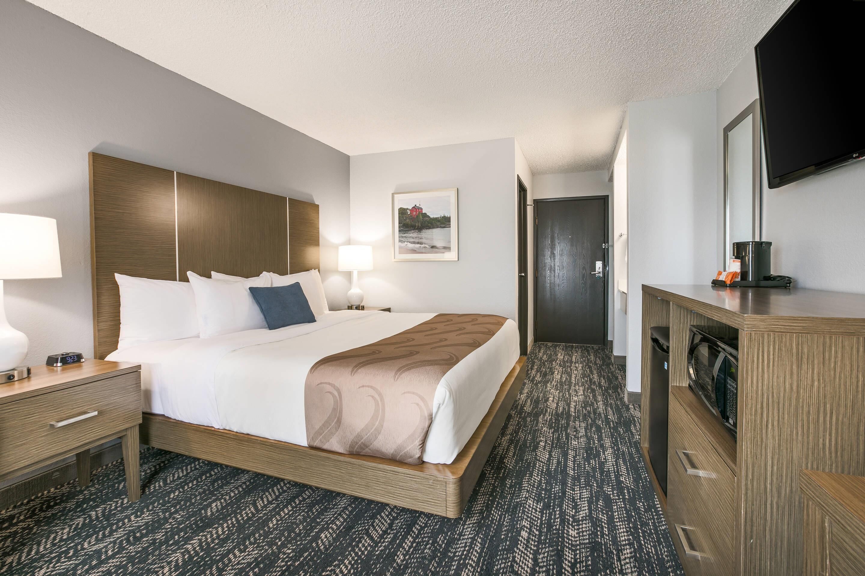 A hotel room with a bed, bedside tables, a TV, a microwave, and a door leading to another room.
