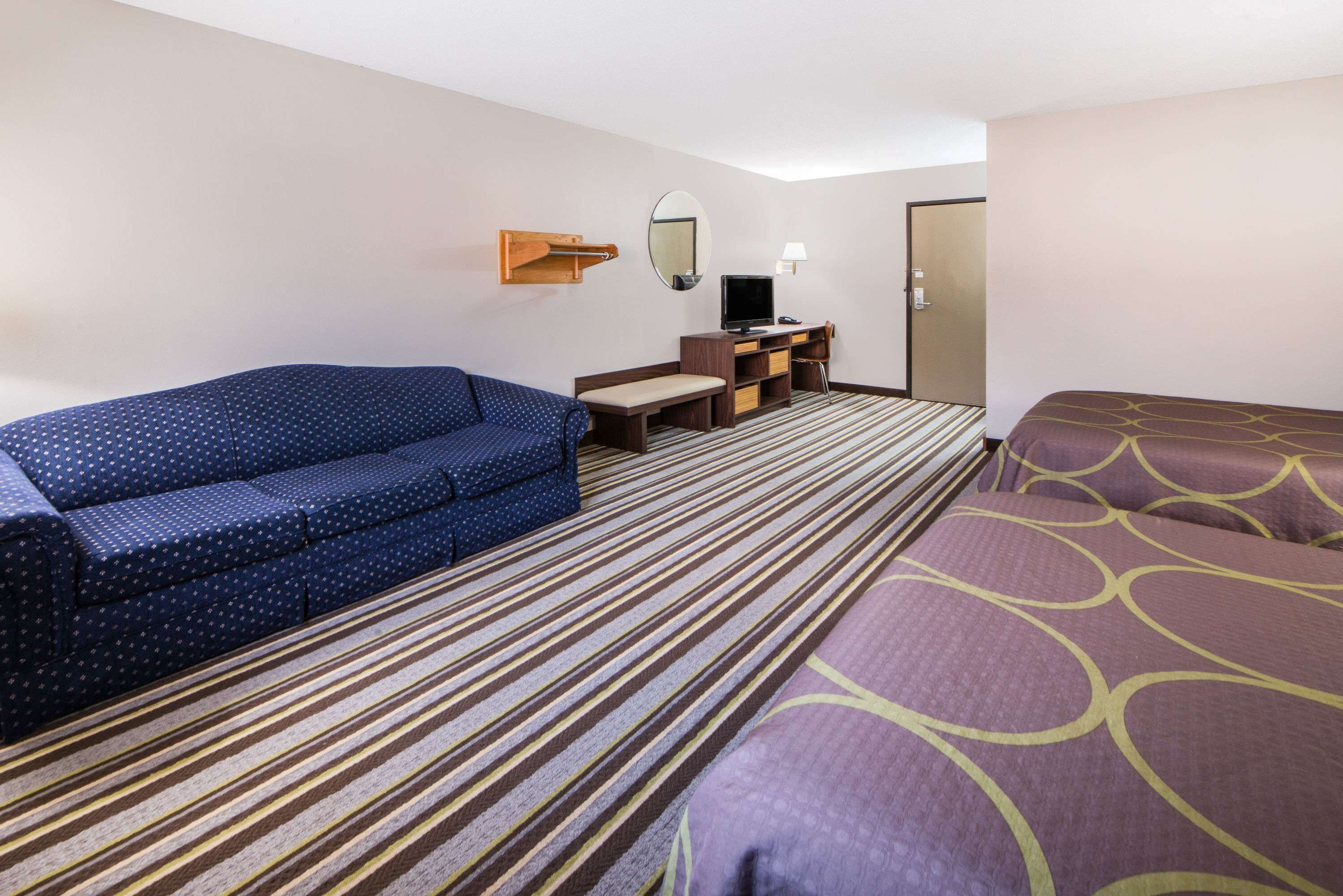 A hotel room with a blue sofa, a bed with a patterned bedspread, a desk with a computer, a mirror, and a striped carpet.