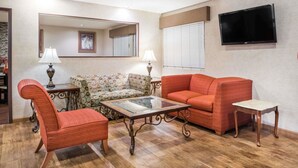 A living room with a sofa, armchair, and coffee table, a television mounted on the wall, and a mirror above the sofa. - Super 8 by Wyndham Lebanon (Lebanon)