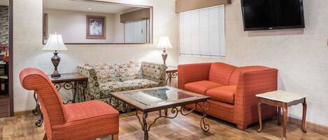 A living room with a sofa, armchair, and coffee table, a television mounted on the wall, and a mirror above the sofa.
