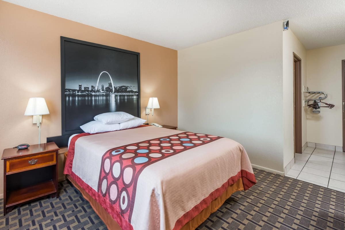 A hotel room with a bed, two bedside lamps, a nightstand, a large cityscape poster, and a door with a coat rack.