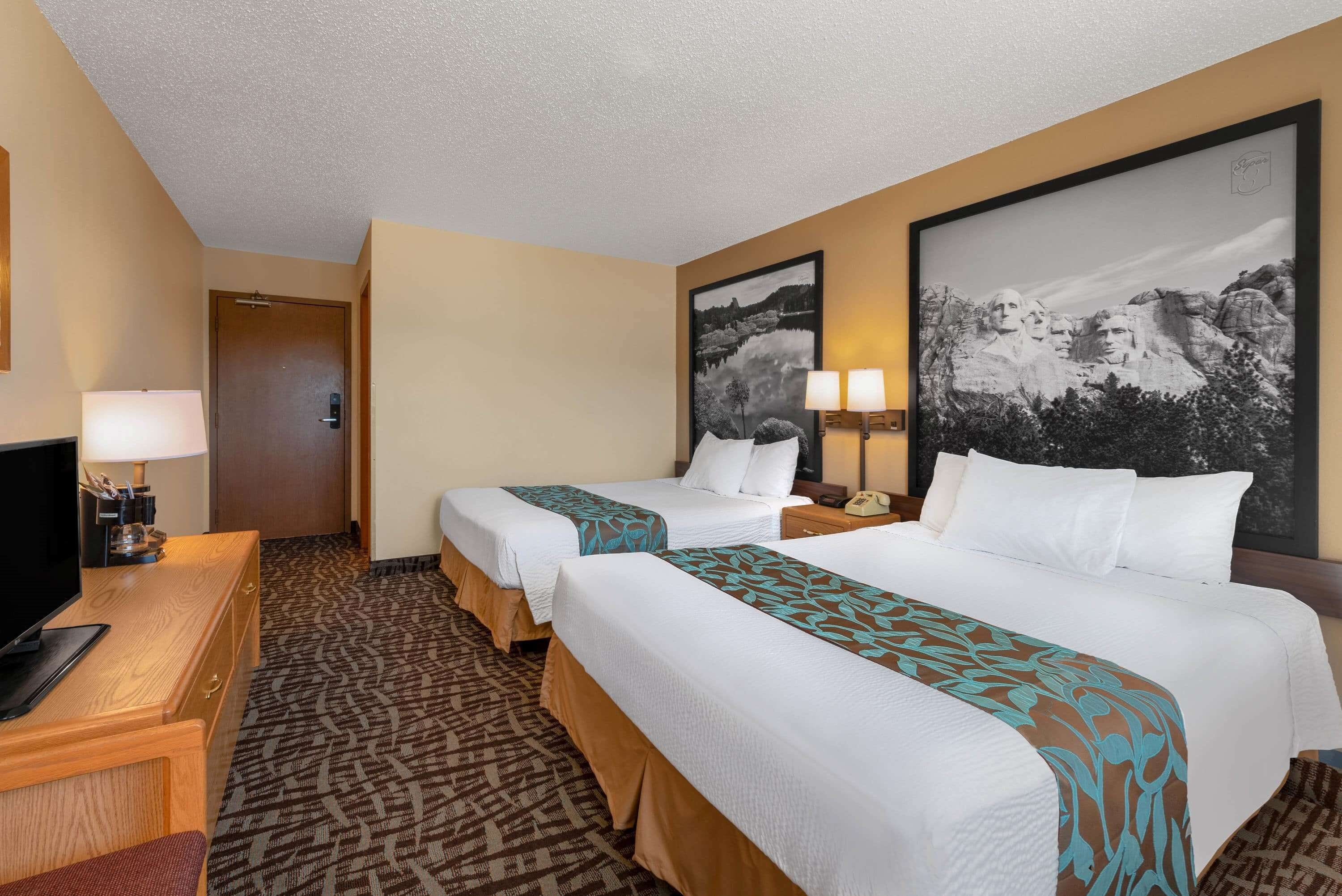 A hotel room with two beds, a desk with a TV, and a large framed picture of a mountain landscape.
