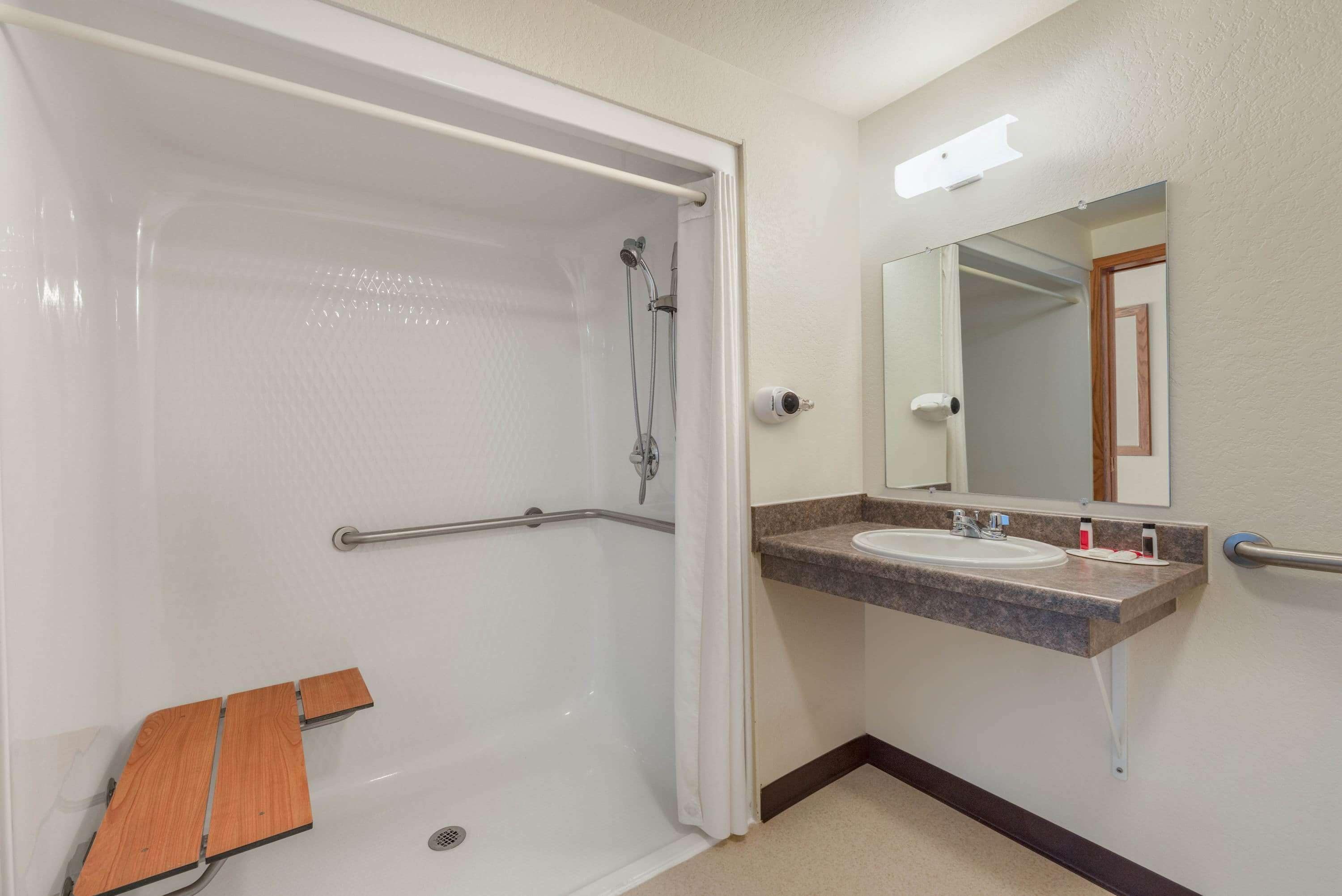 Une salle de bain avec une douche à l’italienne, des barres d’appui, un lavabo avec un miroir et un banc en bois.