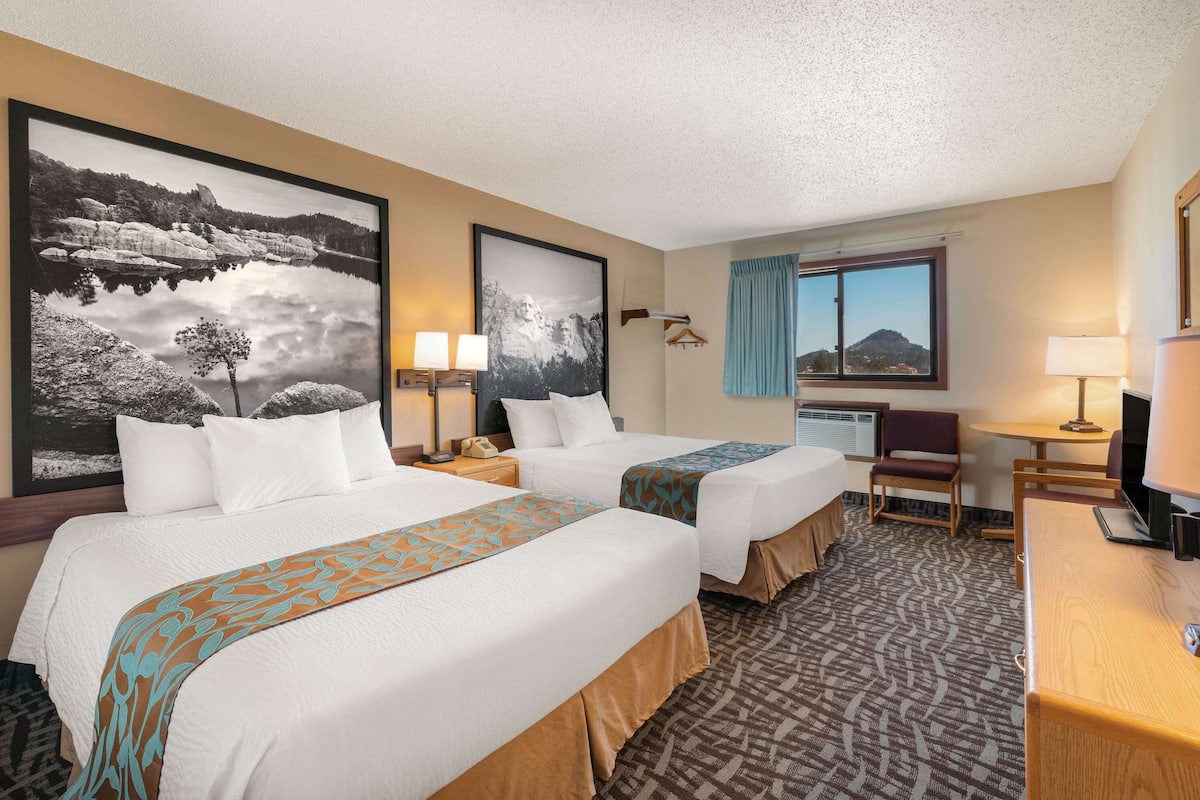 A hotel room with two beds, a desk, a chair, and a large window.