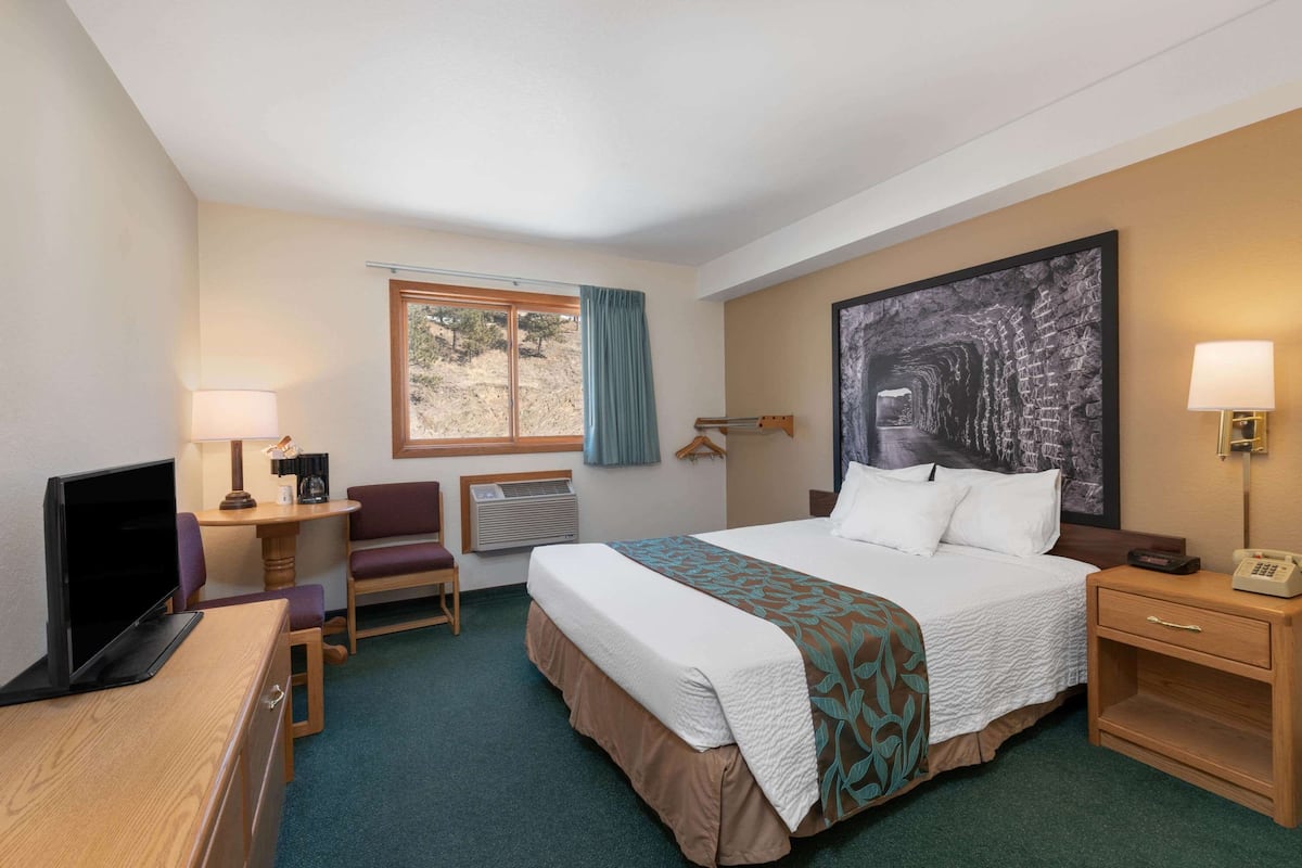 A hotel room with a bed, desk, chair, TV, and a large painting on the wall.