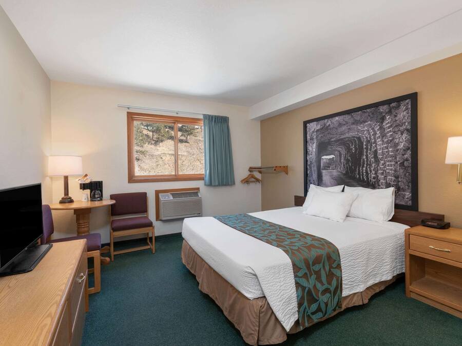 A hotel room with a bed, desk, chair, TV, and a large painting on the wall.