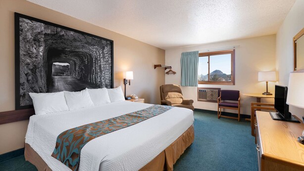 A hotel room with a large bed, a desk with a computer, a chair, a TV, a window with a view, and a large abstract painting on the wall. - Super 8 by Wyndham Hill City/Mt Rushmore/ Area (Hill City)