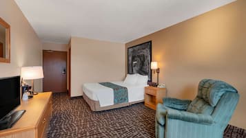 A hotel room with a bed, a desk with a lamp, a chair, and a painting on the wall.