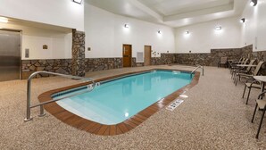 An indoor swimming pool with a stone wall, a wooden deck, and a seating area with chairs. - Super 8 by Wyndham Hill City/Mt Rushmore/ Area (Hill City)