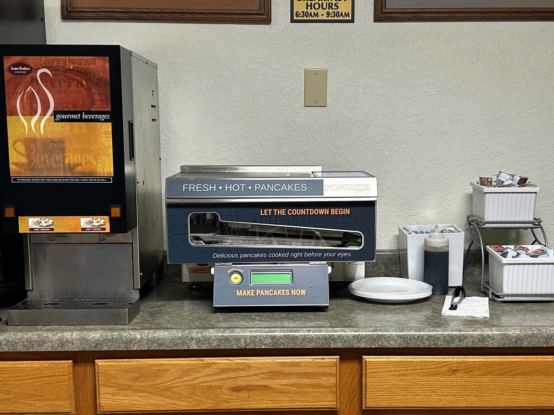 Una estación para el desayuno con una máquina de café, un dispensador de chocolate caliente y un preparador de panqueques.