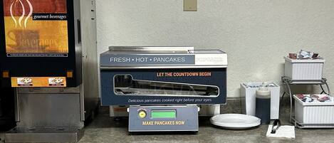 A breakfast station with a coffee machine, a hot cocoa dispenser, and a pancake maker.