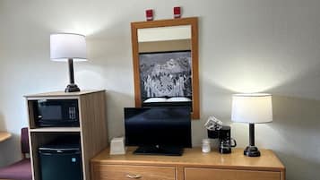 A hotel room with a wooden desk, a television, a microwave, a coffee maker, and a framed picture on the wall.