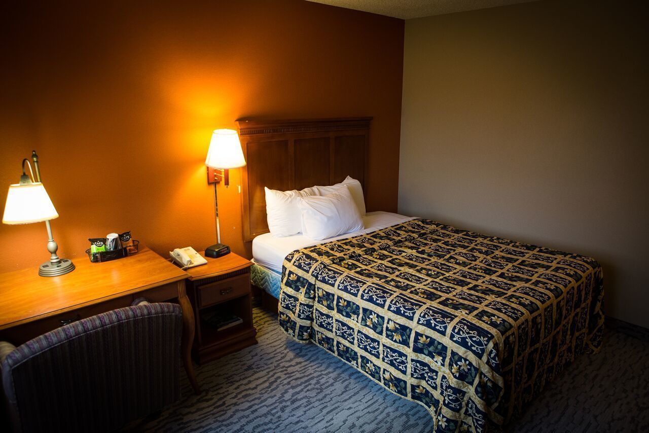 A hotel room with a bed, a desk with a lamp, a chair, and a nightstand.