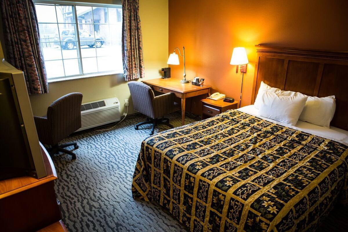 A hotel room with a bed, desk, chair, and a window with curtains.