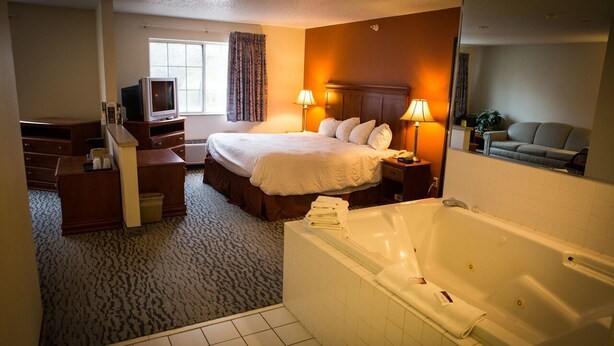A hotel room with a large bed, a sitting area with a sofa, a TV, a desk, and a bathtub.