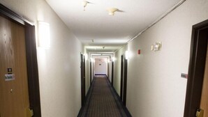 A hotel hallway with carpeted floors, doors on both sides, and ceiling lights.