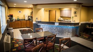 A compact hotel kitchen with a tiled backsplash, wooden cabinets, and a small dining area with a table and chairs.