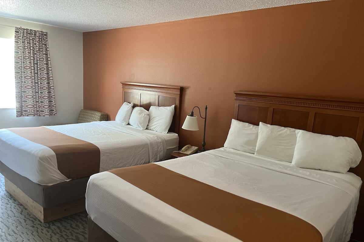 Two double beds with wooden headboards, a patterned curtain, and a bedside lamp.