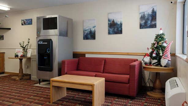 A hotel room with a red sofa, a small wooden table, a water dispenser, a heater, and a Christmas tree with gnome decorations. - Magnuson Hotel Ironwood (Ironwood)