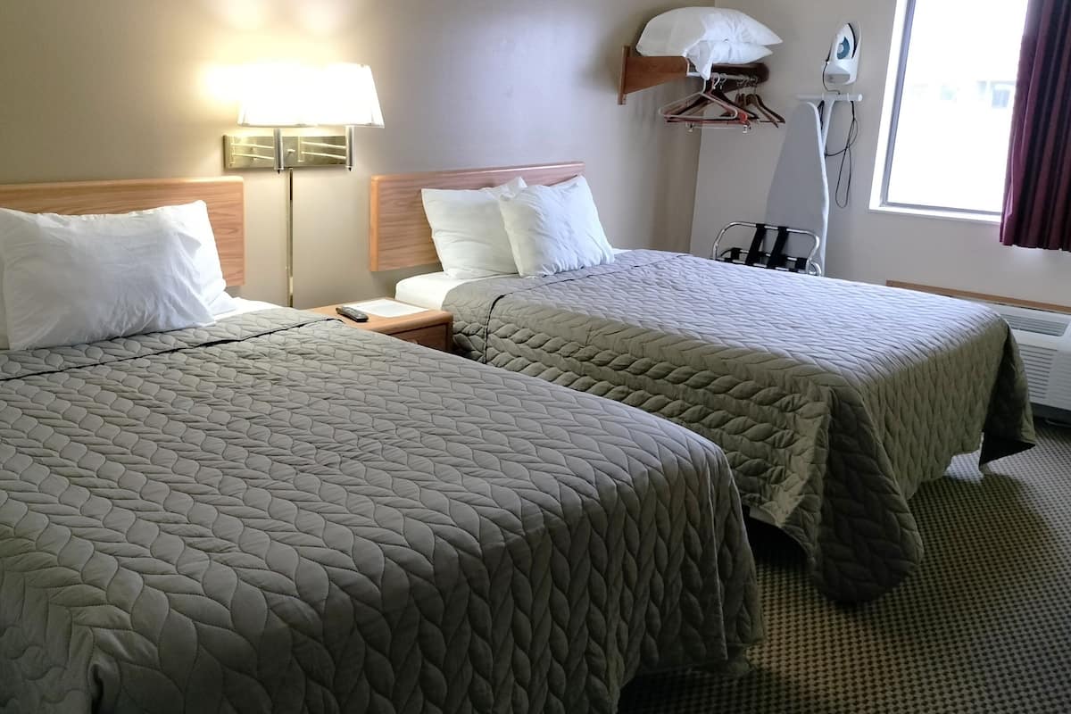 Une chambre d’hôtel avec deux lits, une table de chevet, une lampe, un fer à repasser et une fenêtre avec des rideaux.
