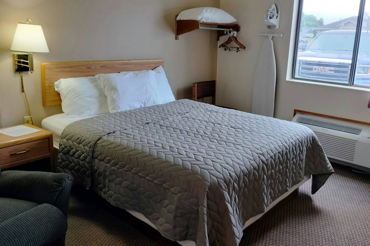 Une chambre d’hôtel équipée d’un lit, d’une chaise, d’une lampe, d’un radiateur et d’une fenêtre donnant sur un véhicule.
