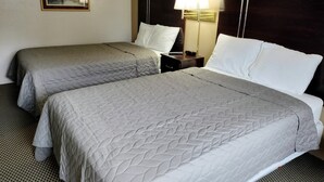 A hotel room with two beds, each with a quilted grey bedspread and white pillows. There is a nightstand with a lamp and a remote control. - Magnuson Hotel Ironwood (Ironwood)