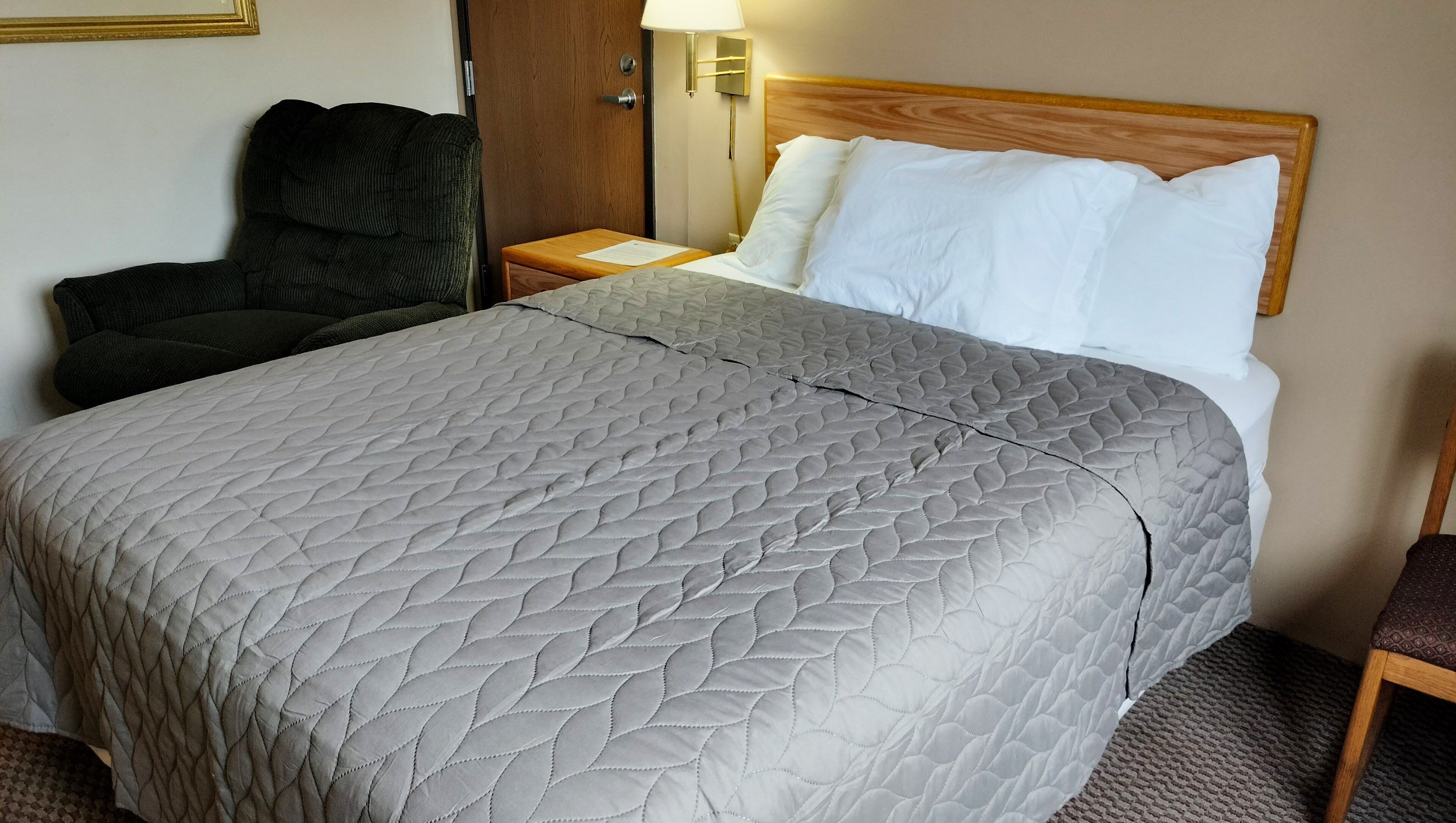 A hotel room with a bed, a nightstand, a lamp, a chair, and a wooden door.