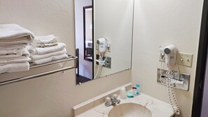 A bathroom with a sink, a towel rack with folded towels, a hairdryer, and a mirror.