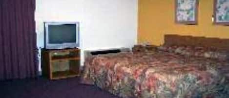 Habitación de hotel con una cama, un televisor sobre un soporte de madera y dos cuadros en la pared.