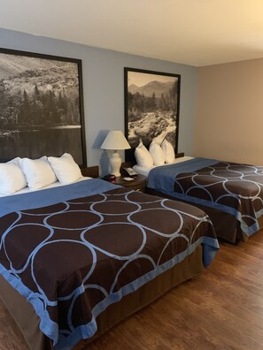 Quarto de hotel com duas camas, uma mesinha de cabeceira, uma luminária e dois quadros na parede.