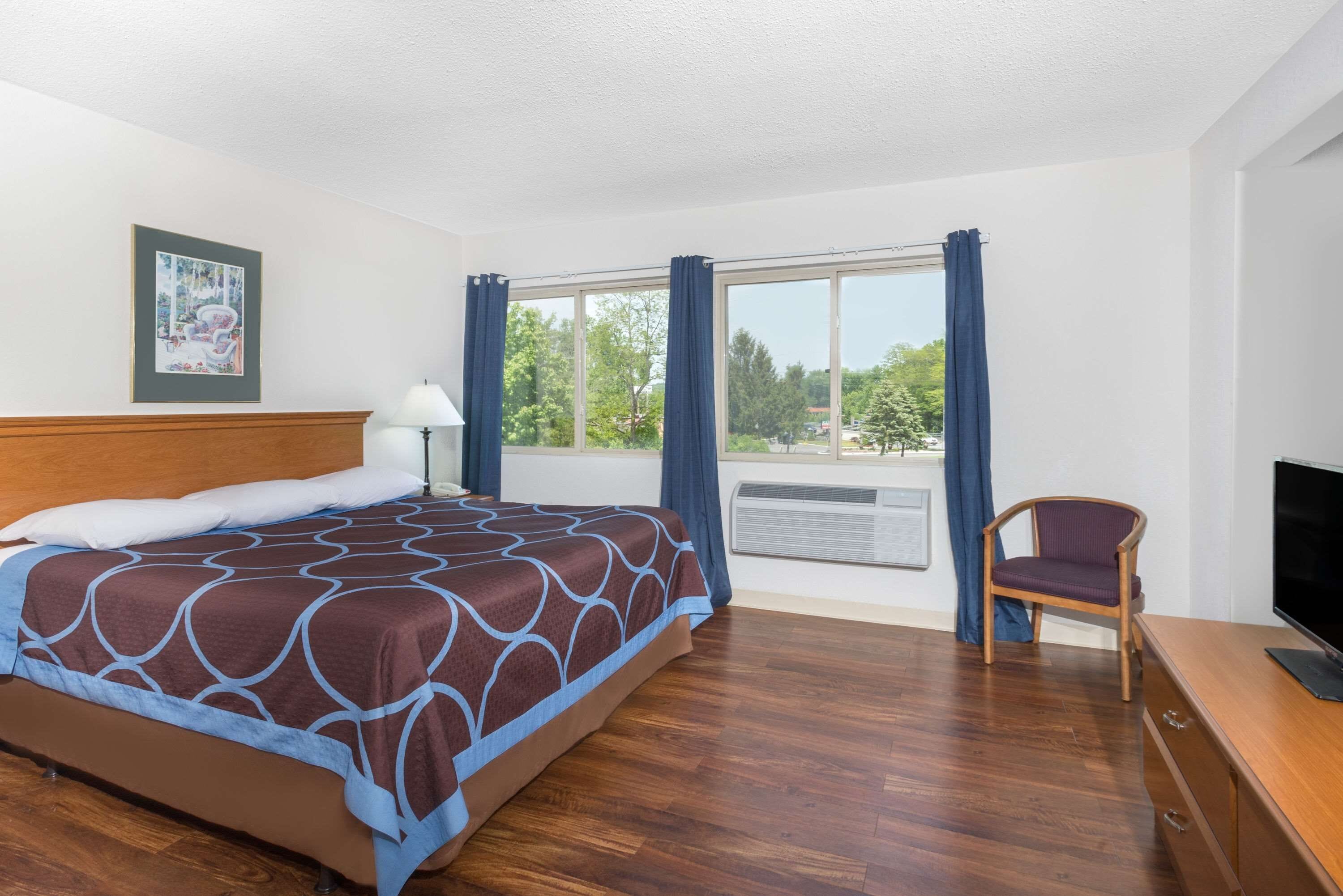 Habitación de hotel con cama, una silla, escritorio con televisor y ventana con cortinas.