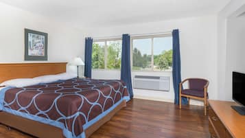 Habitación de hotel con cama, una silla, escritorio con televisor y ventana con cortinas.
