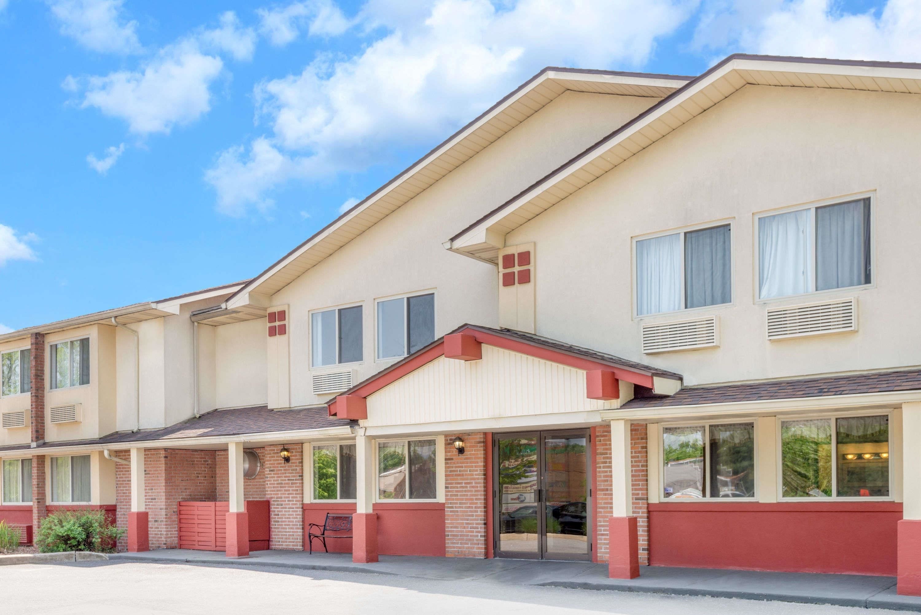 Un motel de varios pisos con fachada color beige y detalles en rojo, que cuenta con un área de estacionamiento techada y una hilera de habitaciones con ventanas amplias.
