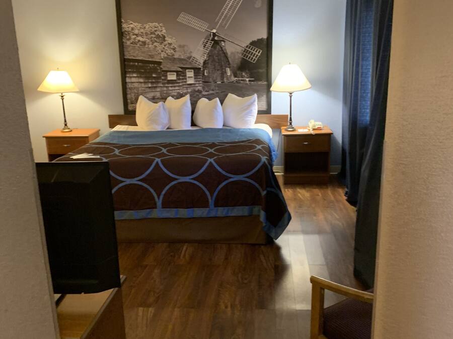 A hotel room with a bed, two bedside tables, a lamp, a chair, and a windmill painting on the wall.