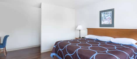 A hotel room with a large bed, a chair, a nightstand with a lamp, and a framed picture on the wall.