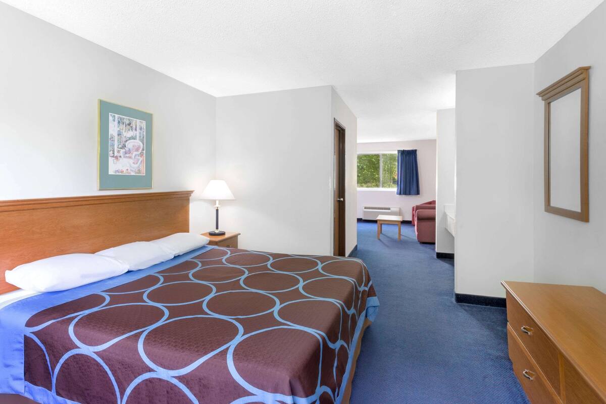 A hotel room with a bed, a nightstand, a lamp, a dresser, and a door leading to a bathroom.